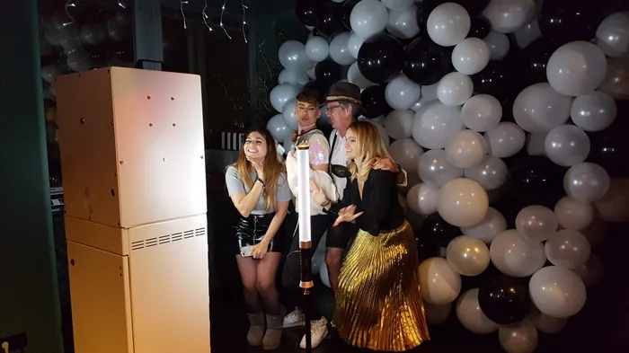 Gruppe von vier Personen posiert ausgelassen vor der SNAPSHOT2GO Fotobox bei einer Party mit schwarz-weißen Luftballons